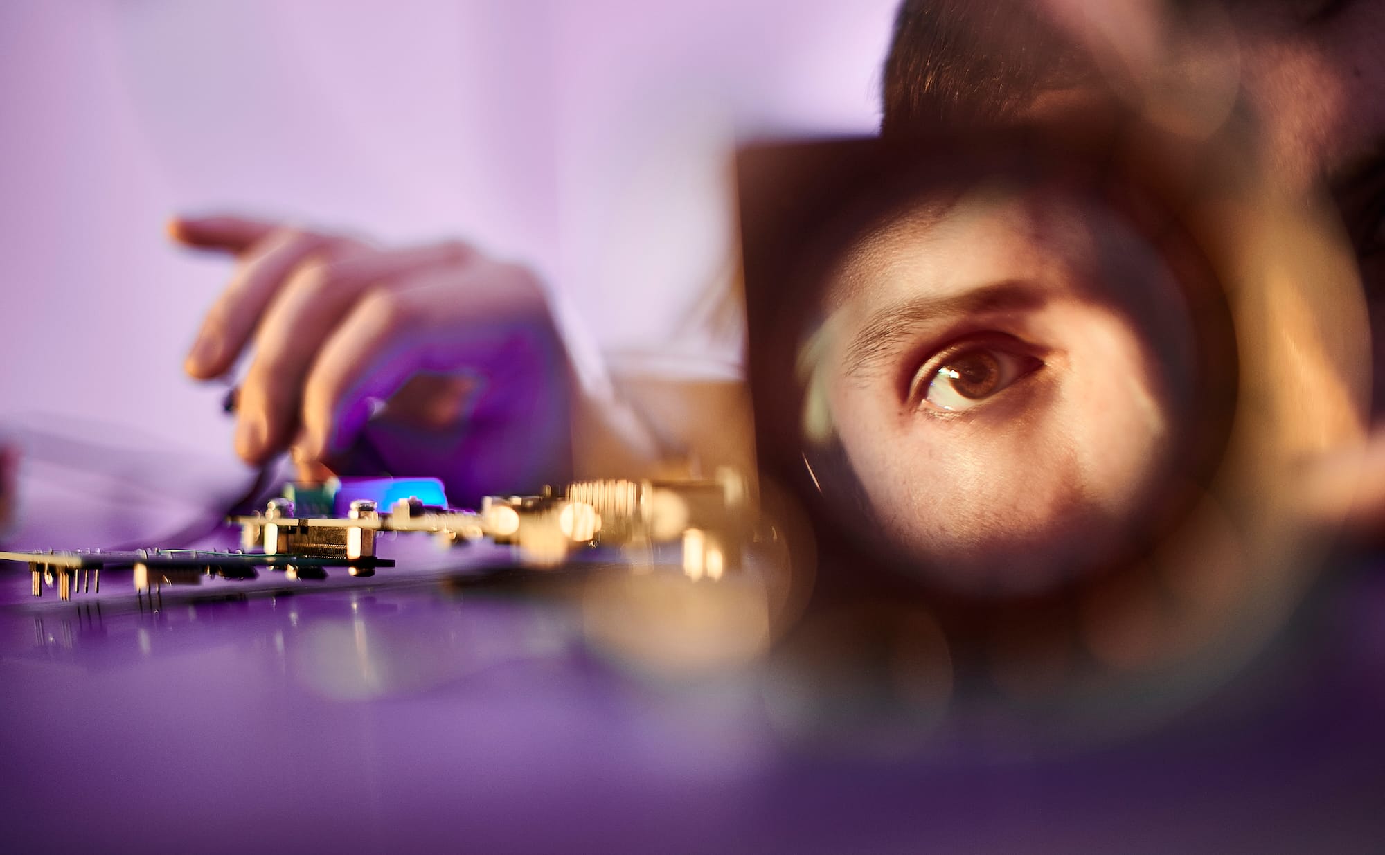 Close-up of a person examining an electronic circuit board through a magnifying lens
