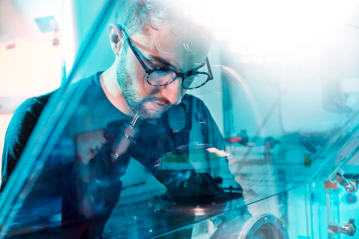 Scientist wearing glasses working with precision tools inside a sealed glovebox in a laboratory