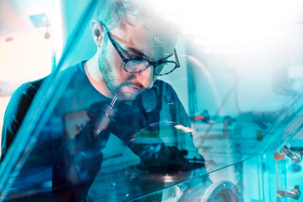 Scientist wearing glasses working with precision tools inside a sealed glovebox in a laboratory