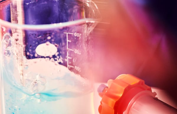 Close-up of a laboratory beaker filled with swirling blue liquid next to a lab connector