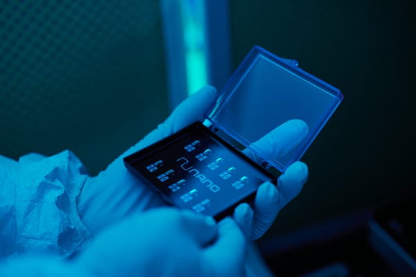 Gloved hands holding an open case labeled 'NuNano', containing precision probes used for atomic force microscopy, in a cleanroom environment